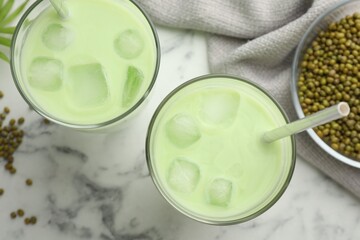 Fresh mung bean juice in glasses and seeds on white marble table, flat lay