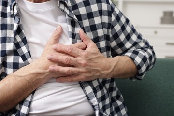 Heart attack. Senior man suffering from pain in chest on sofa at home, closeup
