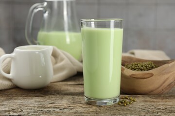 Fresh mung bean juice in glass and seeds on wooden table against grey tiled wall, closeup