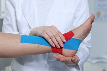 Doctor applying kinesio tapes to patient's foot in hospital, closeup