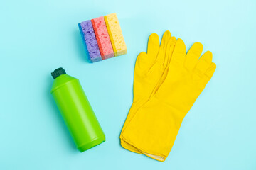 Detergent in a green plastic bottle, sponges and gloves on the table