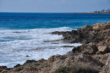 Coastal view showcasing rugged rocky cliffs meeting the vibrant blue ocean waves under a bright sky. Captures the essence of a serene seascape with the natural beauty of untouched shores.