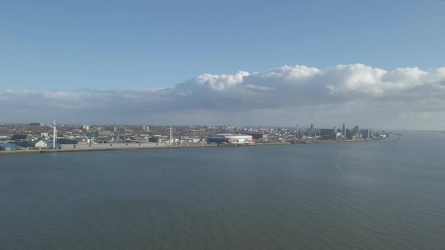 Aerial view of the city of Liverpool from the other side of the river Mersey. Drone moving forwards over the river in direction of the new Everton stadium. Some clouds and blue sky in background.
