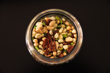 Various types of nuts and seeds in a glass jar close-up, top view. A light snack