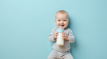 Laughing baby boy holding milk bottle on blue background. Infant nutrition concept. World Breastfeeding Week, National Baby Food Day. Parenting and child care.
