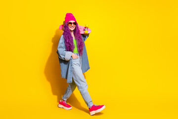 Modern young woman with vibrant outfit and skateboard posing in front of a yellow background