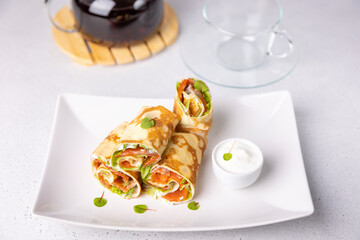 Pancakes with salmon (trout), sour cream, greenstuff and tea. Thin, not sweet blinchiki stuffed with red fish. Traditional Russian and Ukrainian dish. Feast of Maslenitsa. Selective focus, close-up.