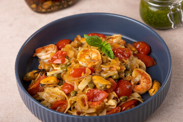 Noodles with shrimps, mussels, tomatoes, onions and capers. Pasta is served with olive oil and pesto sauce. Homemade traditional Mediterranean cuisine. Selective focus, close-up.