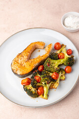 Fried salmon steak (trout) with baked broccoli and cherry tomatoes. Served with sour cream sauce with dill. Traditional home cooking. Selective focus, close-up.