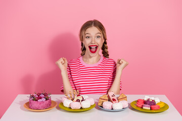 Young woman with braided hair excitedly enjoying a colorful dessert selection against a vibrant pink background