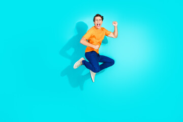 Fototapeta premium Energetic Young Man Jumping Against a Turquoise Background Expressing Happiness and Freedom in Casual Clothing