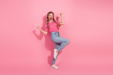Joyful young woman in casual striped t-shirt posing energetically against a pink background,...