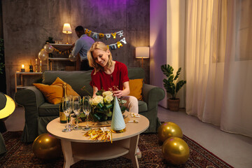 Woman arranging flowers at birthday party with friend preparing drinks