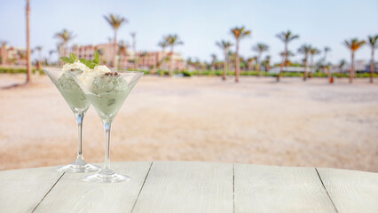 Ice cream in glasses on a table against a background of a tropical sandy beach.