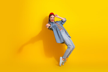 Fashionable young woman in denim outfit posing confidently against a vibrant yellow background,...