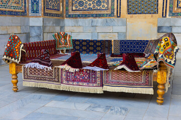 Close-up of wooden tapchan covered with multi-colored carpets with traditional Uzbek floral and...