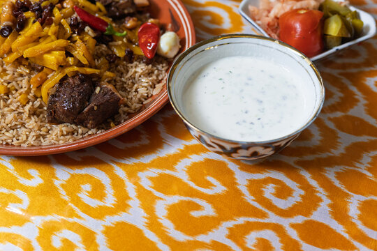 Still life with national Uzbek pilaf and Qatiq with spicy herbs. Tasty pilaf from carrots, chunks of meat and loose rice. Selective focus. Qatiq is a fermented milk product. Background with copy space