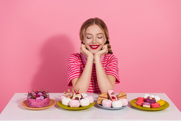 Charming young woman with red lipstick enjoys desserts on a pink background, showcasing fashion and beauty.