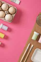 Easter egg painting preparation. Gouache for painting eggs, brushes, palette, glass of water on a pink background. A place for your text.