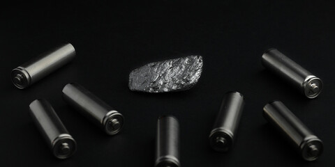 Piece of natural graphite ore, amongst batteries, black background. Mine, mining of critical...
