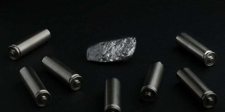 Piece of natural graphite ore, amongst batteries, black background. Mine, mining of critical minerals. Used as anode material in lithium-ion batteries, and other battery technologies