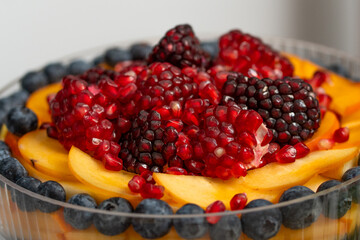 Colorful fruit dessert topped with berries and pomegranate in a clear glass bowl