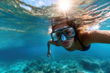 A young woman swims gracefully underwater, showcasing her snorkeling gear while beautifully illuminated by the sunlight filtering through the ocean waves.