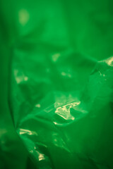 Extreme close up of green empty plastic bag background. The plastic surface is wrinkly and tattered making abstract pattern. Selective focus, shallow depth of field.