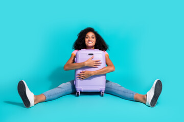 Young woman hugging a stylish purple suitcase with a happy smile against a vibrant cyan background