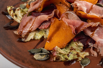Delicious autumn salad with prosciutto, roasted pumpkin, beets, lettuce, and balsamic glaze on a rustic plate. Gourmet, colorful, and healthy meal