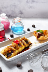 Pisang goreng keju (Fried banana with grated cheese) garnished with Pandan leaf served on a white plate above wooden table. Top view close up details 04