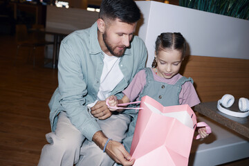 Dutch angle shot of father embracing daughter who looking into paper bag while unpacking it, they...