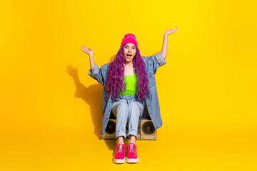 Trendy young woman in vibrant outfit posing playfully against bright yellow background, expressing energy and style with dyed hair