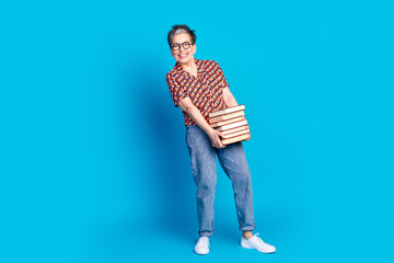 Stylish mature woman holding stack of books, smiling confidently against a vibrant blue background,...