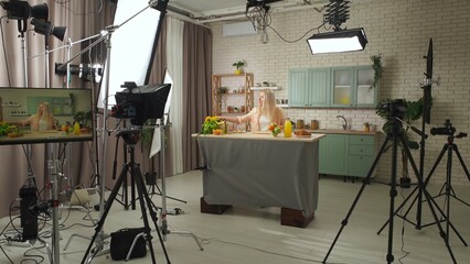 Woman host in the kitchen at the table preparing breakfast, talking and smiling, backstage video recording of a tv program in the professional studio.