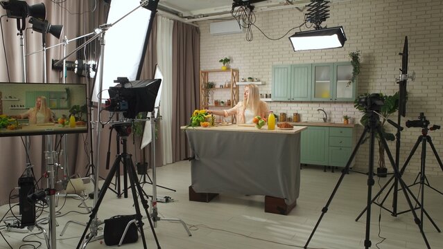 Woman host in the kitchen at the table preparing breakfast, talking and smiling, backstage video recording of a tv program in the professional studio.