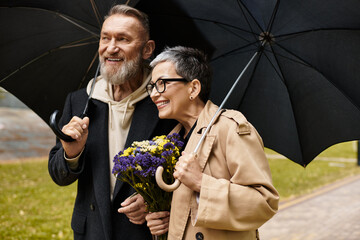 Mature couple enjoying a romantic stroll under umbrellas with a bouquet of flowers