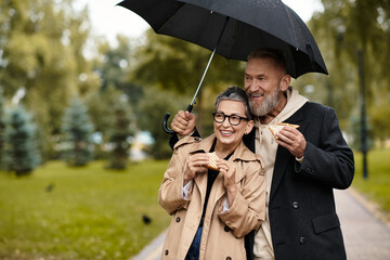 Mature couple sharing joy under an umbrella while enjoying treats in the park © LIGHTFIELD STUDIOS