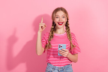 Young woman with braids in striped t-shirt holds smartphone and points up against pink background