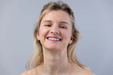 A Bright and Cheerful Young Woman with a Natural Smile and Light Blonde Hair Against a Soft Gray...