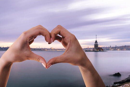 Hands form a heart shape against a stunning Istanbul sunset with Maiden Tower in the background.