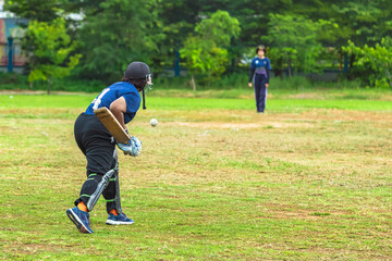 Asian young female cricket player wear protective gear and hitting ball with bat on field. Woman teenager playing cricket in park. Girl with bat and ball on cricket pitch. Sports activity and exercise