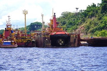 An orange and red tugboat with an oversized propeller on the dry dock. Next to it, other pilot...