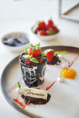 Thiramisu dessert plate with a chocolate cake and strawberries. The plate is white and the dessert is topped with chocolate sauce