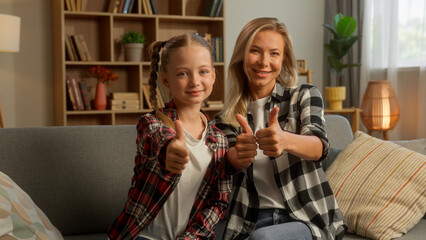 Carefree glad Caucasian parent female little kid girl demonstrating thumb up at home mother schoolgirl child showing approval daughter smile family successful symbol woman mom yes gesture achievement