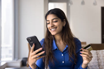 Young woman holding smartphone and credit card, smiling, engaged in online transaction or purchase, doing on-line shopping or making electronic payment, enjoy secure, convenient money transfer via app
