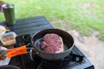 Grilled meat on hot pan for making steak or barbecue during camping. man is grilling meat on a pan over a picnic gas stove after going camping to increase the convenience of grilling meat and speed.