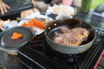 Grilled meat on hot pan for making steak or barbecue during camping. man is grilling meat on a pan over a picnic gas stove after going camping to increase the convenience of grilling meat and speed.