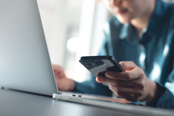 Business woman working on laptop computer and using mobile phone at office. Woman typing on laptop and using smartphone searching the information, surfing the internet on office table