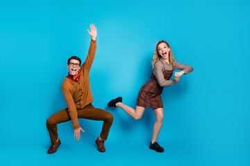 Young couple in retro outfits posing joyfully against vibrant blue background
